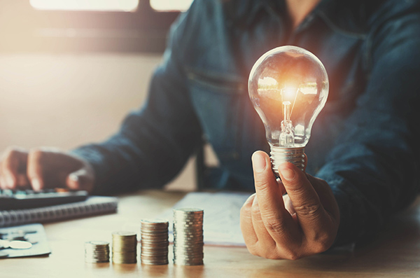 Coins stacked from smallest to largest in-front of a man holding a lightbulb